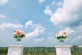 Site for the wedding ceremony outdoor. Fresh flowers in glass vases stand on white tables against blue sky with white clouds Royalty Free Stock Photo