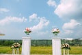 Site for the wedding ceremony outdoor. Fresh flowers in glass vases stand on white tables against blue sky with white clouds Royalty Free Stock Photo