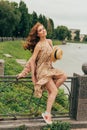 sits on a fence, in the hands of a hat, a beige dress in a flower and a beige sweater.beautiful red-haired girl.picture against th Royalty Free Stock Photo