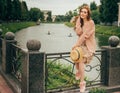 Sits on a fence, in the hands of a hat, a beige dress in a flower and a beige sweater.beautiful red-haired girl.picture against th Royalty Free Stock Photo