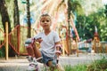 Sits on the green grass. Cheerful little girl on roller skates have a good time in the park near attractions Royalty Free Stock Photo