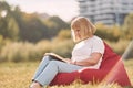 Sitting on the armchair and reading the book. Senior woman having nice weekend outdoors on the field at sunny day Royalty Free Stock Photo