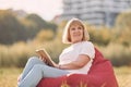 Sitting on the armchair and reading the book. Senior woman having nice weekend outdoors on the field at sunny day Royalty Free Stock Photo