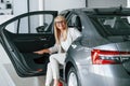 Sitting in automobile`s seat. Woman in white formal clothes is in the car dealership