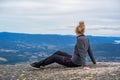 Sitting blonde woman in gray and black sports clothing enjoying the view of a valley and hills.