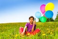 Sitting boy with flying balloons in summer