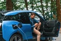 Sitting with doors opened. Handsome man is waiting for his electric car to charge, outdoors Royalty Free Stock Photo