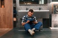 Sitting on the floor with notepad in hands. Plumber in blue uniform is at work in the bathroom