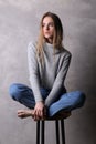 Sitting girl in sweater with crossed legs. Gray background Royalty Free Stock Photo