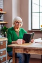 Septuagenarian dame sitting at kitchen table with Bible in hands