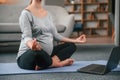 Sitting in lotus pose. With laptop. Beautiful pregnant woman is indoors at home Royalty Free Stock Photo