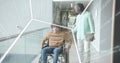 Sitting man in wheelchair in brown sweater, jeans getting support in corridor, tablet, code overlay Royalty Free Stock Photo