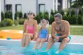 Parents and daughter sitting near swimming pool on hot summer day Royalty Free Stock Photo