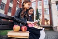 Sitting and reading. Two schoolgirls is outside together near school building Royalty Free Stock Photo