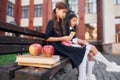 Sitting and reading. Two schoolgirls is outside together near school building Royalty Free Stock Photo