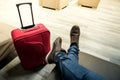 Sitting with the red suitcase in the airport waiting room. Detail of the feet and luggage. Above photography Royalty Free Stock Photo