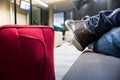 Sitting with the red suitcase in the airport waiting room. Detail of the feet and luggage. Lounge with lounge chairs Royalty Free Stock Photo