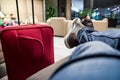 Sitting with the red suitcase in the airport waiting room. Detail of the feet and luggage.Lounge with lounge chairs Royalty Free Stock Photo