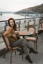 Sitting sideways turned Parisian young woman in restaurant terrace. Portrait of stylish young woman wearing autumn coat