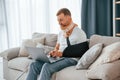 Sitting on the sofa with laptop. Man with crutches is at home indoors. Having injuries Royalty Free Stock Photo