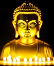 Sitting statue of smiling buddha with lighted candles. Golden buddha glowing holy colorful light.