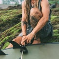 Sitting surfer with tattoos, dreadlocks close up