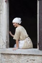 Pretty young girl in period medieval costume, an actress playing the role of washerwoman, sitting at the window