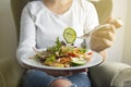 Sitting woman hold and eating vegan salad with arugula, celery and spinach in white plate. Healthy eating Royalty Free Stock Photo