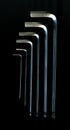 Six chrome-plated metal l-shaped furniture keys octagonal cross-section on a black background. Royalty Free Stock Photo