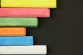 Six colored children crayons on black background, on left side, blue red green yellow orange white, top view Royalty Free Stock Photo