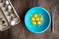 Six cracked eggs in blue mixing bowl, whole eggs in cardboard carton, metal whisk, wood table