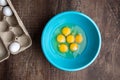 Six cracked eggs in blue mixing bowl, whole eggs in cardboard carton, wood table