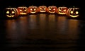 Six creepy Halloween grinning pumpkins glow in the dark with reflections on the floor. 3d rendering