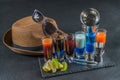 six different colored shot drinks, lined up on a black stone plate, ice cubes in shaker and ice tongs, lemon and lime, brown Royalty Free Stock Photo