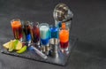 six different colored shot drinks, lined up on a black stone plate, ice cubes in shaker and ice tongs, lemon and lime Royalty Free Stock Photo