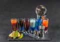 six different colored shot drinks, lined up on a black stone plate, ice cubes in shaker and ice tongs, lemon and lime Royalty Free Stock Photo