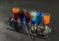 six different colored shot drinks, lined up on a black stone plate, ice cubes in shaker and ice tongs, black sunglasses Royalty Free Stock Photo