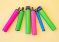 Six electronic vape cigarettes of different colors and sizes lie on a yellow background