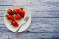 Six fresh juicy strawberries on a plate with a fork lying on a blue wooden table Royalty Free Stock Photo