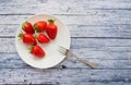 Six fresh juicy strawberries on a plate with a fork lying on a blue wooden table Royalty Free Stock Photo