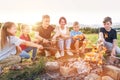 Six kids group Boys and girls cheerfully laughed and roasted sausages on sticks over a campfire flame near the green tent. Outdoor