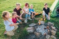 Six kids group Boys and girls cheerfully laughed and roasted sausages on sticks over a campfire flame near the green tent. Outdoor Royalty Free Stock Photo