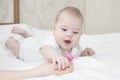 The six-month-old baby girl lies on her stomach and pulls her hand to the nipple. A small child in white looks at the pacifier.