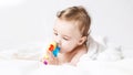 Six months old baby wearing a towel after a bath. Baby care concept. Cute toddler playing with rattle on white bed. toddler gnaws Royalty Free Stock Photo