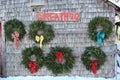 Six natural Christmas wreaths decorated with festive bows hanging on the side of a wood shingled barn.