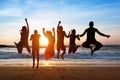 Six people jumping on beach at sunset.