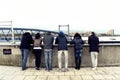 Six people watching the ferry and Woolwich Arsenal Pier in London.