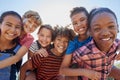 Six pre-teen friends piggybacking in a park, close up portrait