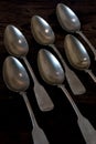 Six silvver spoons lying in a staggered row on wooden table