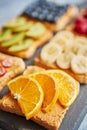 Six toasts with peanut butter, fresh fruits on a grey slate